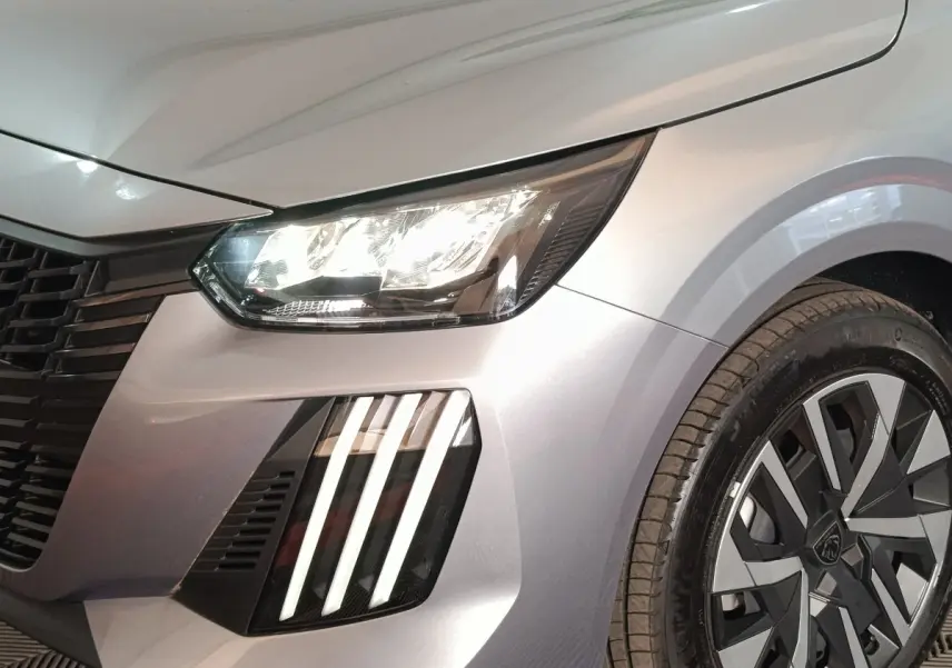 Gros plan sur l'avant droit gris clair d'une Peugeot 208 Hybrid 100 e-DCS6 avec phares LED et jante stylisée.
