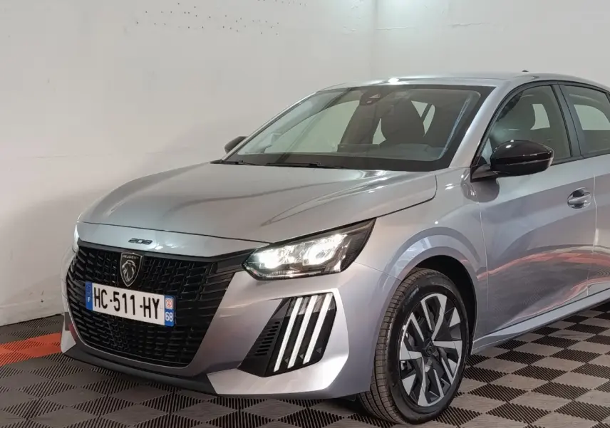 Peugeot 208 Hybrid gris clair vue 3/4 avant droit, phares LED allumés et jantes distinctives bicolores.