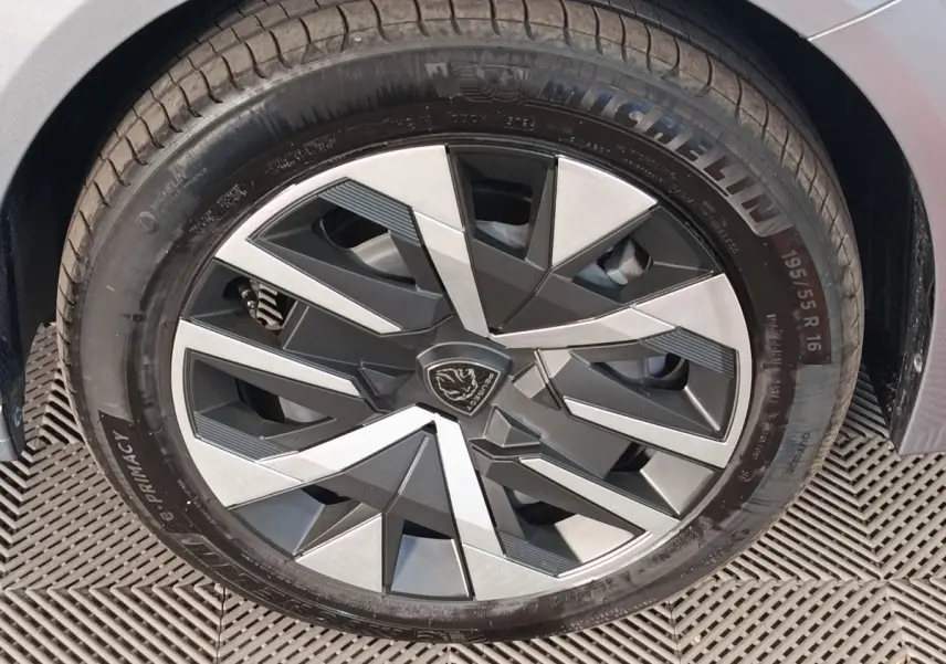 Gros plan sur la roue avant droite d'une Peugeot 208 Hybrid gris clair avec jante au design géométrique bicolore.