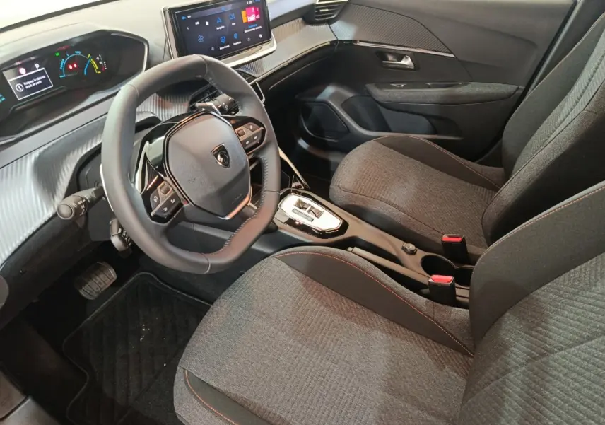 Vue intérieure côté conducteur de la Peugeot 208 Hybrid 2025, volant cuir multifonctions et sièges tissu gris avec surpiqûres rouges.