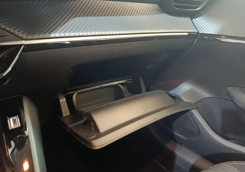Vue intérieure du coffre à gants ouvert sur le côté passager d’une Peugeot 208 Hybrid gris clair, tableau de bord avec finition carbone.