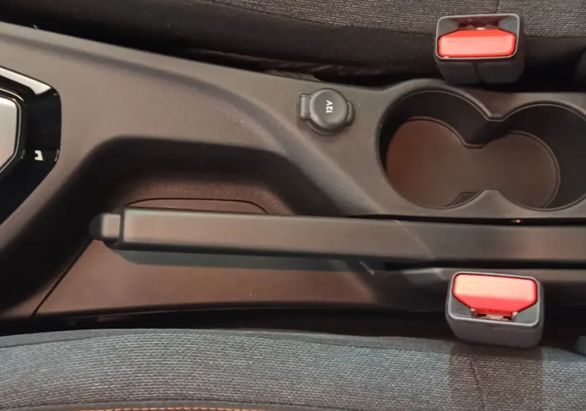 Vue rapprochée de la console centrale de la Peugeot 208 Hybrid 2025, avec frein à main, prise 12V et porte-gobelets noirs.