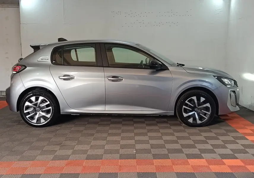 Profil droit d'une Peugeot 208 Hybrid gris clair 2025 avec jantes modernes et badge Style sur l'aile arrière.