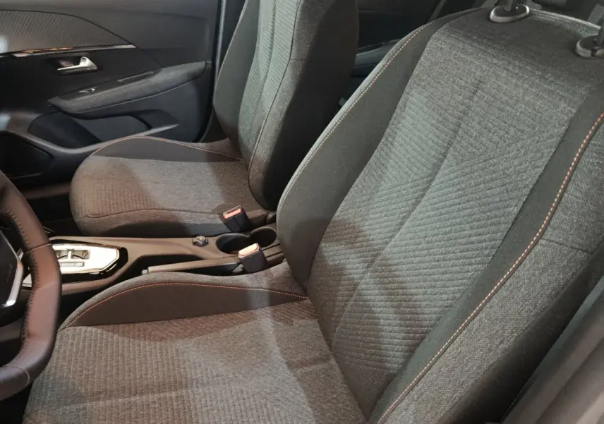 Vue intérieure rapprochée des sièges avant gris foncé avec surpiqûres orange de la Peugeot 208 Hybrid 2025.