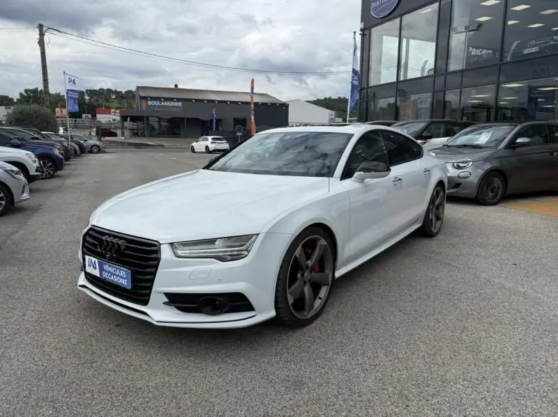 Audi A7 Sportback blanc vue 3/4 avant droit, jantes noires et étriers de frein rouges visibles, devant un showroom.