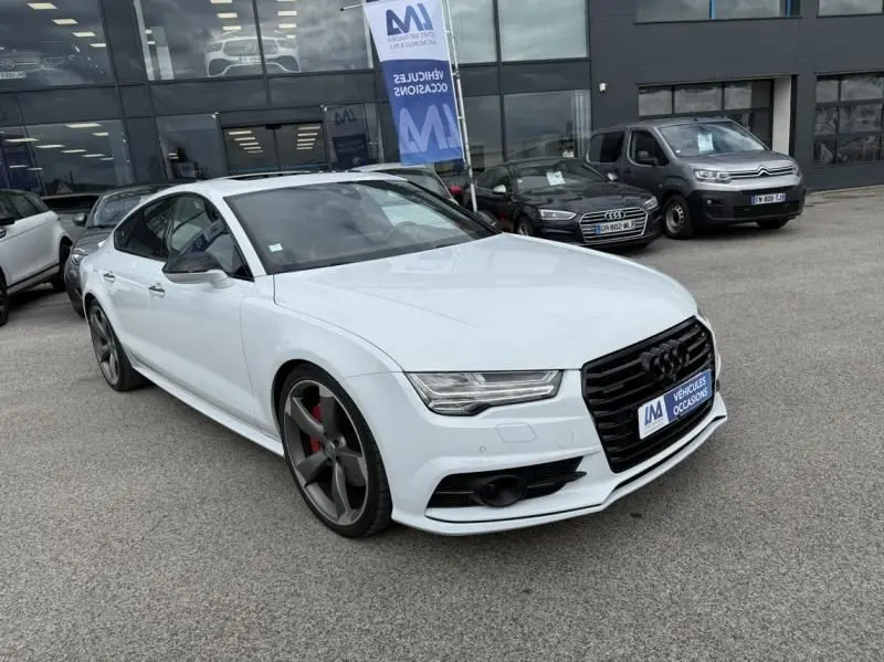 Audi A7 Sportback blanc vue 3/4 avant droit, jantes grises avec étriers rouges, devant un showroom.