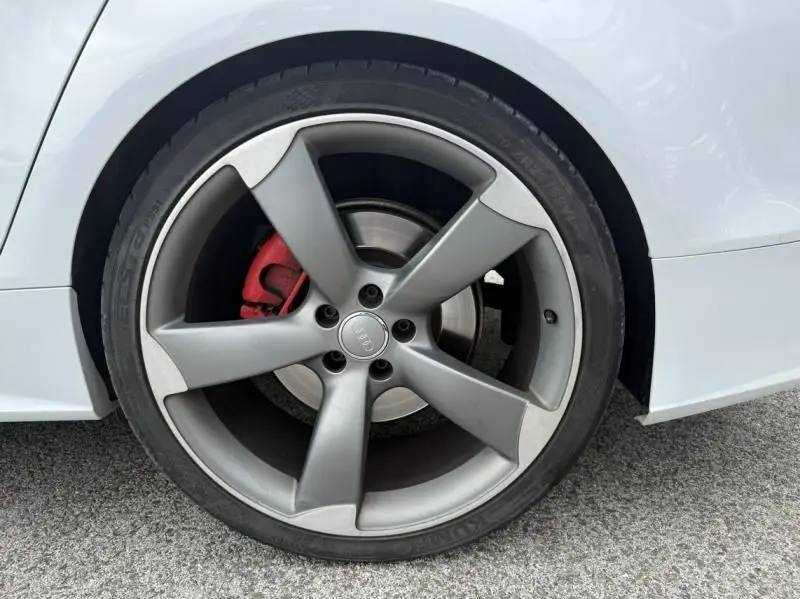 Gros plan sur la roue avant droite d'une Audi A7 Sportback blanche, avec étrier de frein rouge visible.