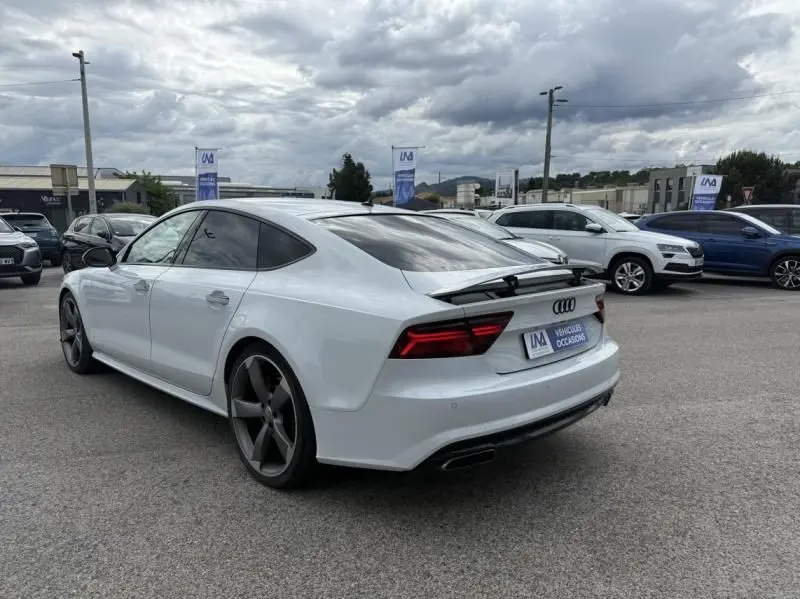 Audi A7 Sportback blanc vue 3/4 arrière droit avec jantes noires et aileron déployé sur parking.