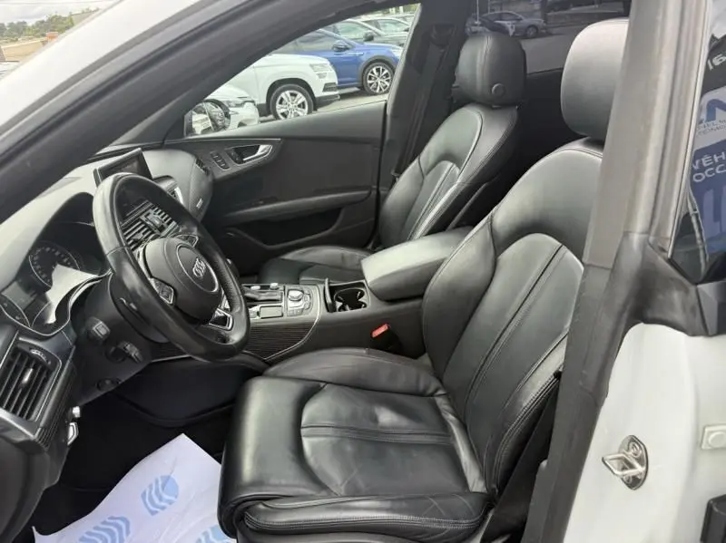 Intérieur de l'Audi A7 Sportback blanc 2018, vue côté conducteur, sièges cuir noir et tableau de bord moderne.
