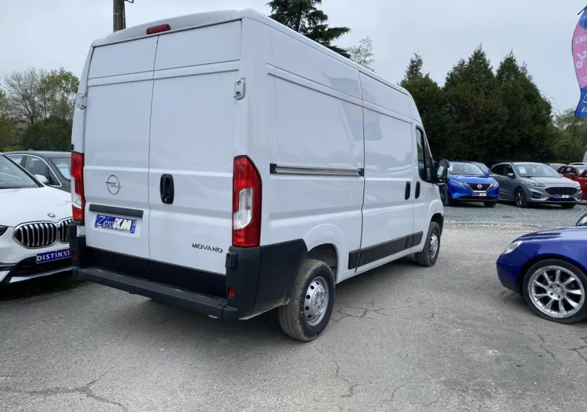 Vue 3/4 arrière droite d'un Opel Movano Fourgon blanc avec portes arrière fermées sur un parking.
