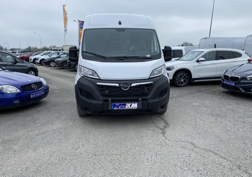 Vue frontale d'un fourgon Opel Movano blanc 2022 avec calandre noire et plaque "Zero KM" sur un parking.