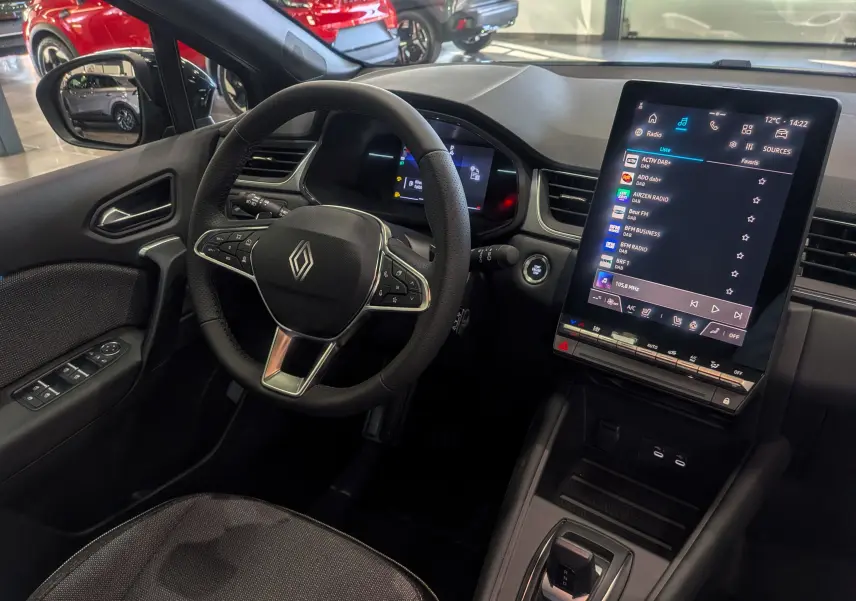 Intérieur du Renault Captur 2025 montrant le volant, la console centrale avec écran tactile vertical et sièges en tissu noir.