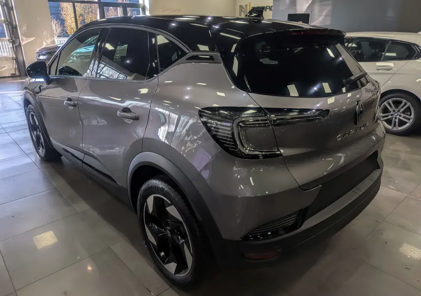 Renault Captur 2025 gris Cassiopé avec toit noir, vue 3/4 arrière droit en intérieur showroom.