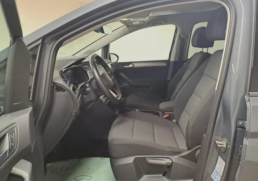 Vue intérieure côté conducteur du Volkswagen Touran gris Dauphin 2024, sièges tissu et tableau de bord moderne.