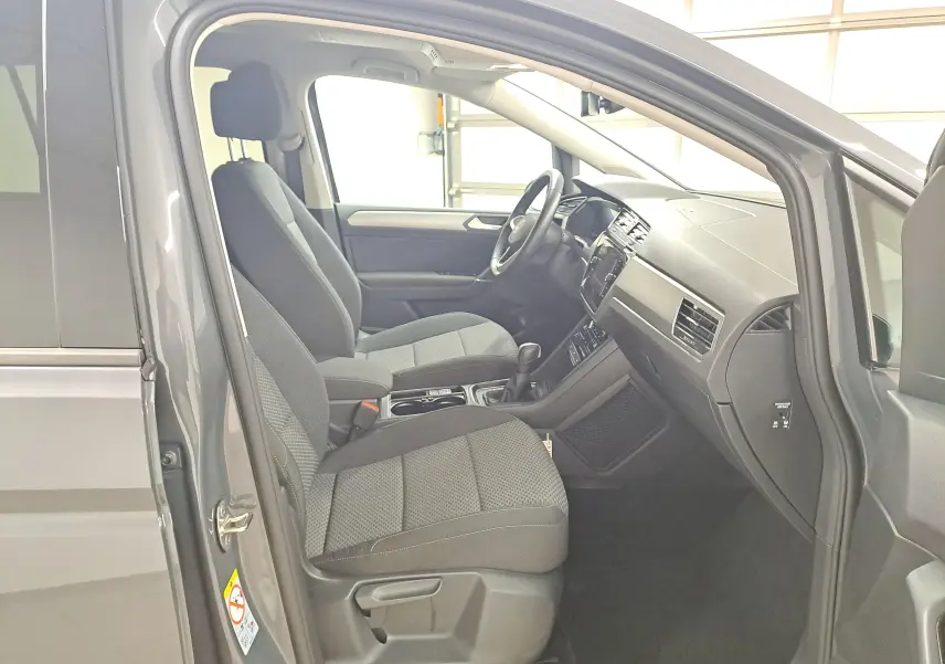 Vue intérieure côté conducteur du Volkswagen Touran gris Dauphin 2024, montrant les sièges avant et le tableau de bord.