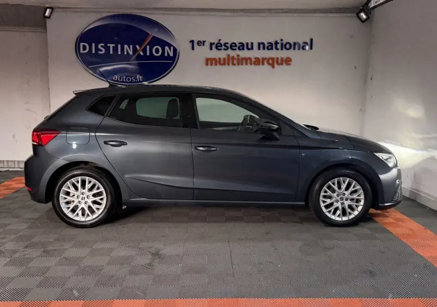 Vue de profil côté gauche d'une SEAT Ibiza 1.0 TSI 110 FR gris foncé, avec jantes alliage et phares allumés.