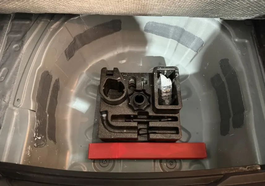 Vue plongeante sur le coffre ouvert d'une SEAT Ibiza gris foncé, montrant le rangement outils et espace pour roue de secours.