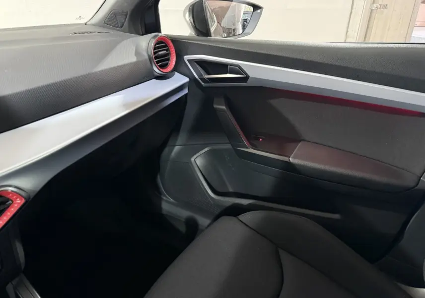 Intérieur côté passager de la SEAT Ibiza 2024 gris foncé, avec aérateurs rouges et garnitures argentées.