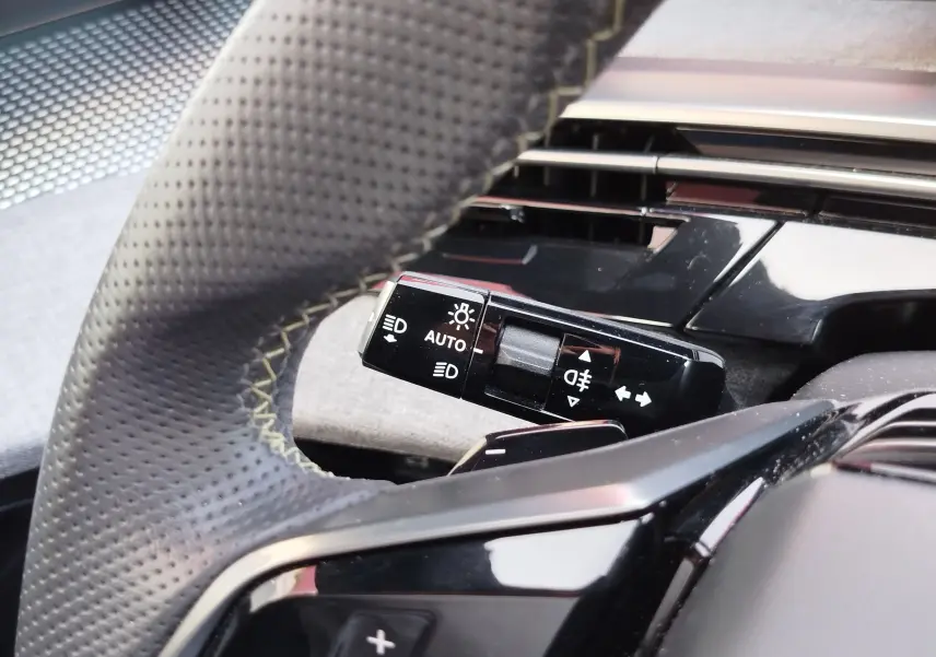 Gros plan sur la commande des phares et clignotants à gauche du volant perforé dans le Peugeot 3008 Bleu Obsession 2024.