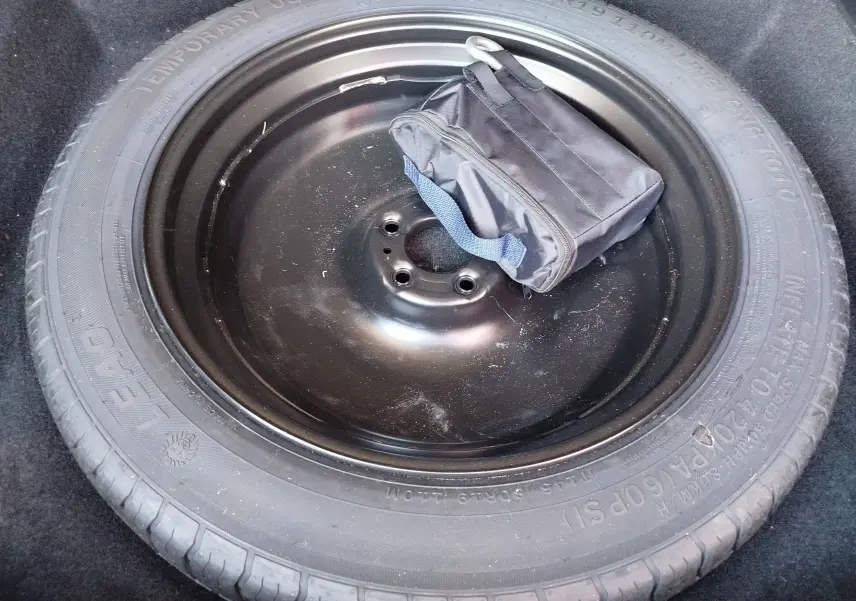 Gros plan sur la roue de secours noire avec une trousse à outils posée dessus dans le coffre du Peugeot 3008 Bleu Obsession.