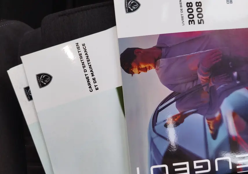 Image ne montrant pas le véhicule mais des brochures Peugeot 3008 et 5008 posées sur un siège, avec un fond sombre.