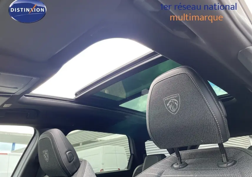 Vue intérieure du Peugeot 5008 Hybrid 136ch GT 2025, sièges avant noirs avec logo Peugeot et toit ouvrant panoramique.