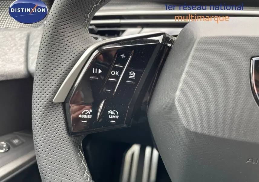 Gros plan sur les commandes au volant perforé du Peugeot 5008 Hybrid 136ch GT 2025 blanc Okenite avec toit noir.