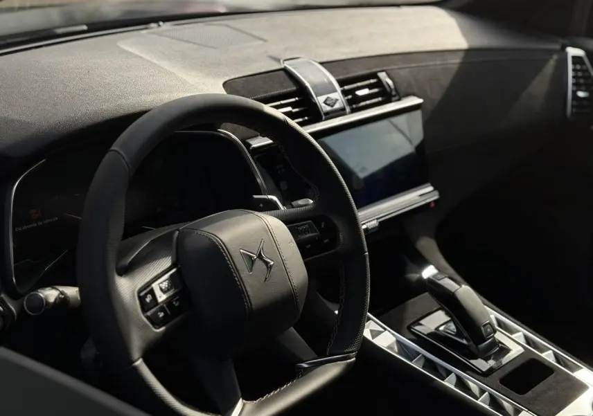 Intérieur du DS7 2025 vu côté conducteur, volant cuir noir avec surpiqûres, console centrale et écran tactile visibles.