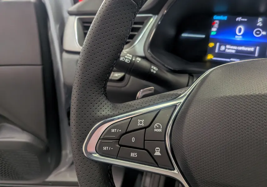 Gros plan sur le volant perforé du Renault Captur 2025 avec commandes intégrées et tableau de bord numérique en arrière-plan.