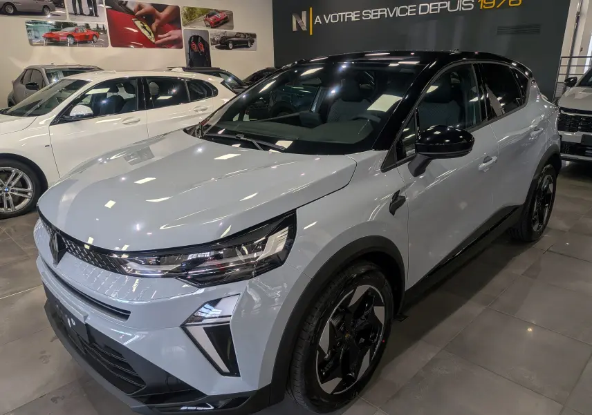 Renault Captur Mild Hybrid 2025 gris Rafale avec toit noir, vue 3/4 avant droit en showroom lumineux.