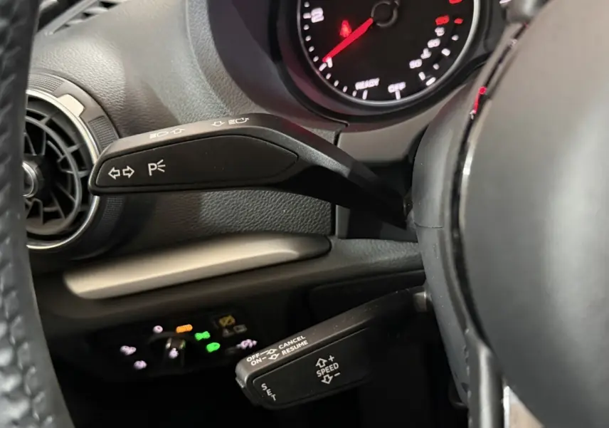 Vue rapprochée du volant noir et des commandes de clignotants et régulateur de vitesse d’une Audi A3 bleu 2018.