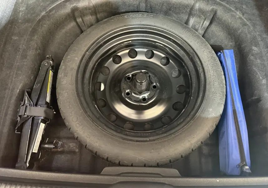 Gros plan sur la roue de secours galette noire dans le coffre de l'Audi A3 2.0 TDI bleu, avec cric et trousse à outils.