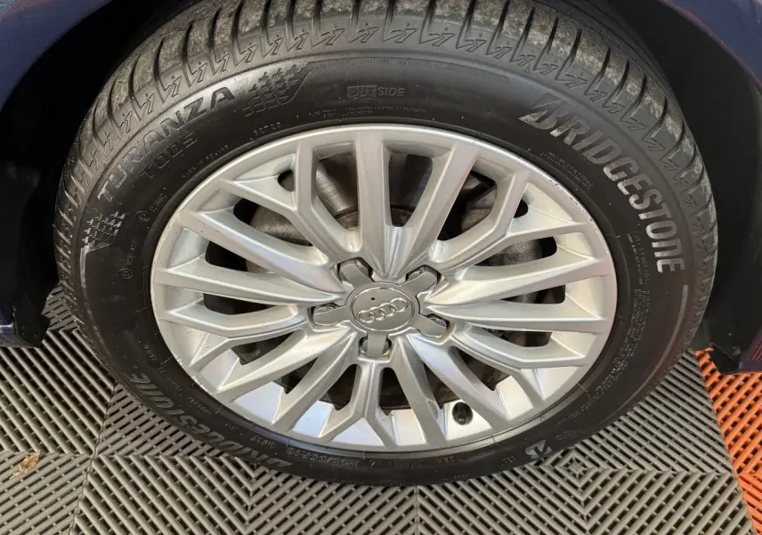 Gros plan sur la roue avant gauche d'une Audi A3 bleu, jante alliage argentée avec logo Audi au centre.