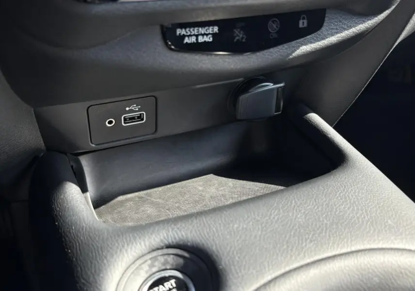 Gros plan sur la console centrale noire du Nissan Juke 2024 avec prise USB, prise 12V et bouton Start/Stop visible.