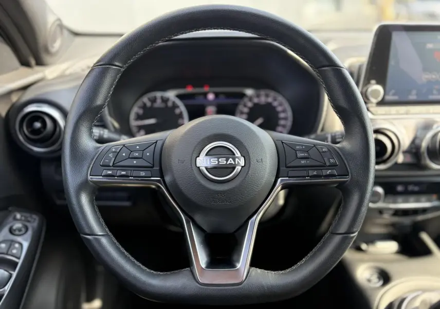Volant en cuir noir de Nissan Juke 2024 avec commandes intégrées, tableau de bord et écran tactile en arrière-plan flou.