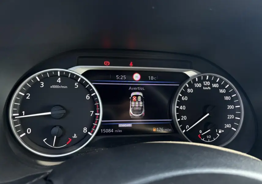 Vue rapprochée du tableau de bord du Nissan Juke 2024, affichant les compteurs et un avertissement sur l'écran central.