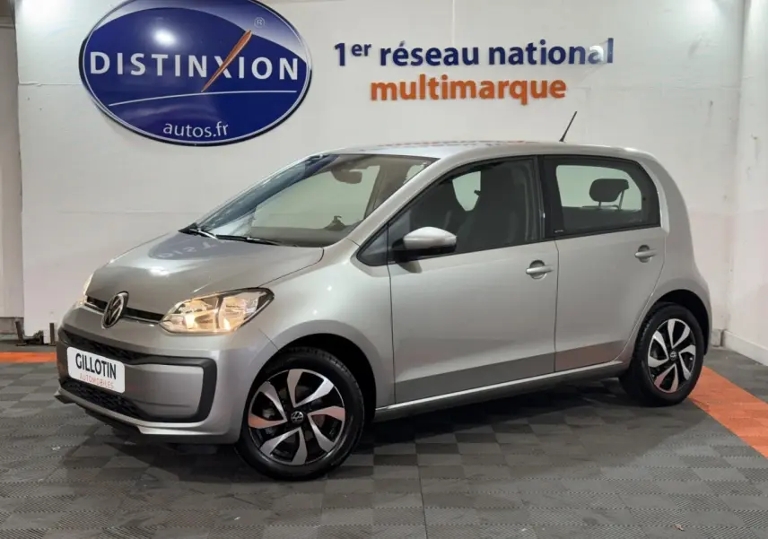 Volkswagen Up gris foncé vue 3/4 avant droit, phares allumés et jantes noires et argentées design moderne.