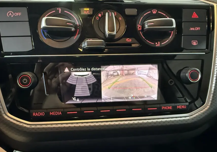 Vue rapprochée du tableau de bord de la Volkswagen Up 1.0 65 Active 2022, montrant l'écran de caméra de recul et les commandes de climatisation.