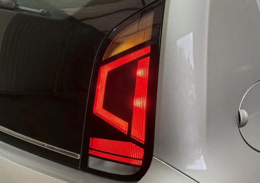 Gros plan sur le feu arrière droit rouge et orange d'une Volkswagen Up gris foncé, avec la trappe à carburant visible.