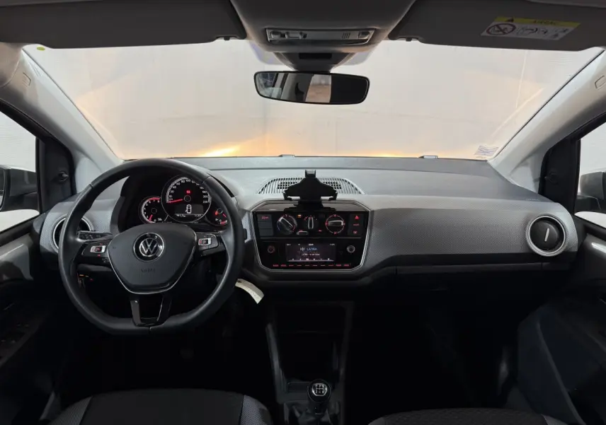 Vue intérieure frontale du tableau de bord gris clair et noir du Volkswagen Up 1.0 65 Active avec volant cuir et boîte manuelle.