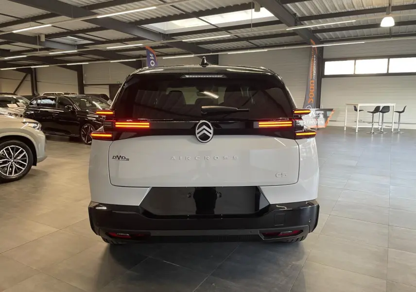 Vue arrière d'un Citroën C5 Aircross blanc Okenite avec toit noir et feux arrière LED allumés en intérieur showroom.
