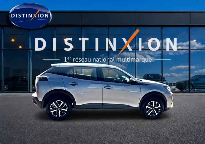 Peugeot 2008 gris en profil droit, avec jantes noires et toit blanc devant une vitrine Distinxion.