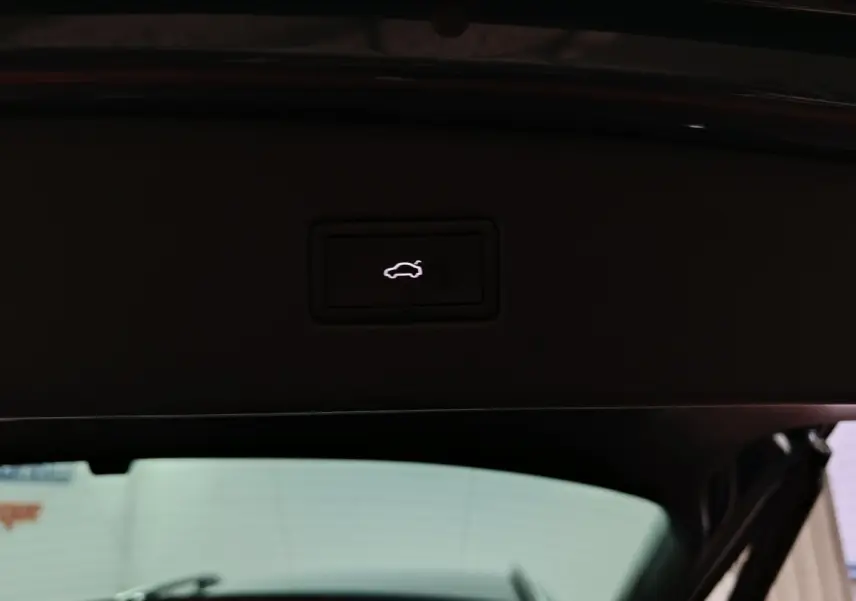 Bouton d'ouverture électrique du coffre visible sur le hayon intérieur d'un Volkswagen Tiguan bleu, vue arrière ouverte.