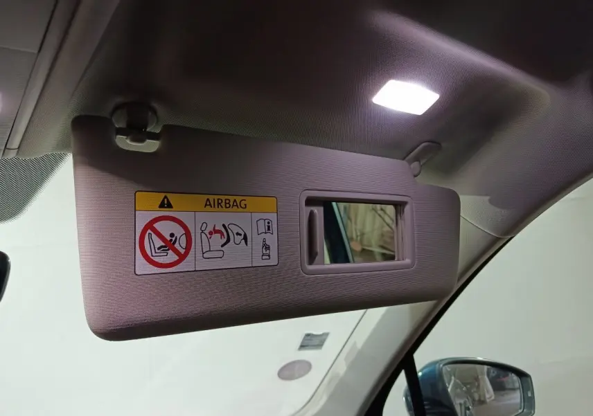 Vue intérieure sur le pare-soleil côté conducteur beige avec miroir et avertissement airbag, rétro extérieur bleu visible.