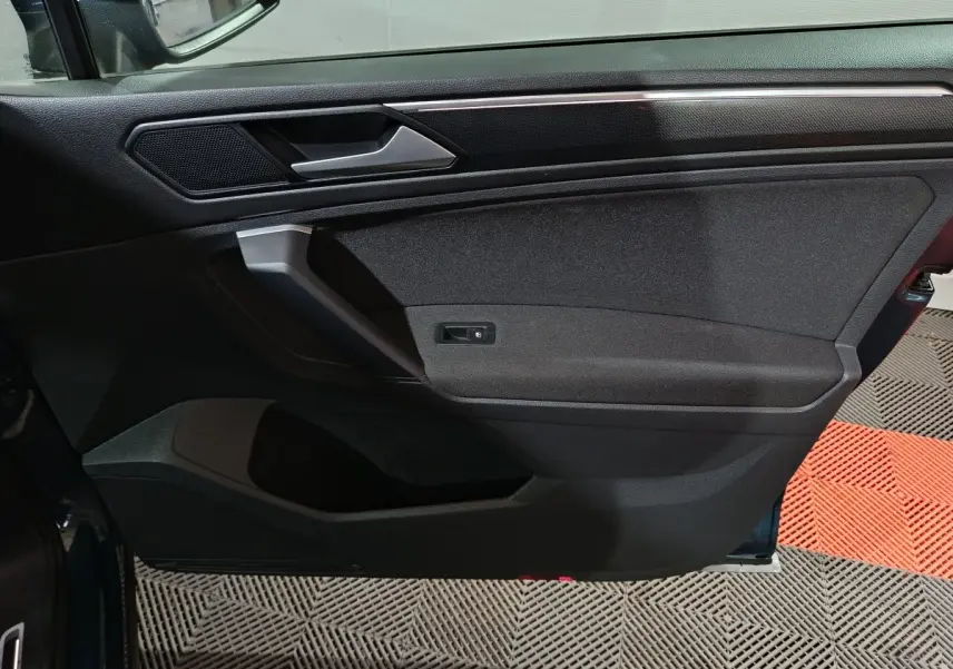 Vue intérieure de la porte avant gauche du Volkswagen Tiguan bleu, avec poignée argentée et panneau noir texturé.