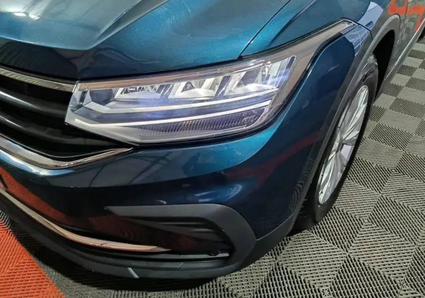 Gros plan sur l'avant droit bleu métallisé du Volkswagen Tiguan 1.5 TSI avec phares LED et calandre chromée.