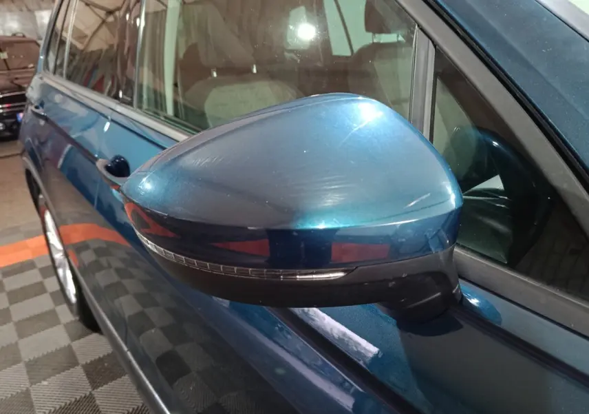 Vue rapprochée du rétroviseur côté conducteur bleu métallisé du Volkswagen Tiguan 2021, avec clignotant intégré.