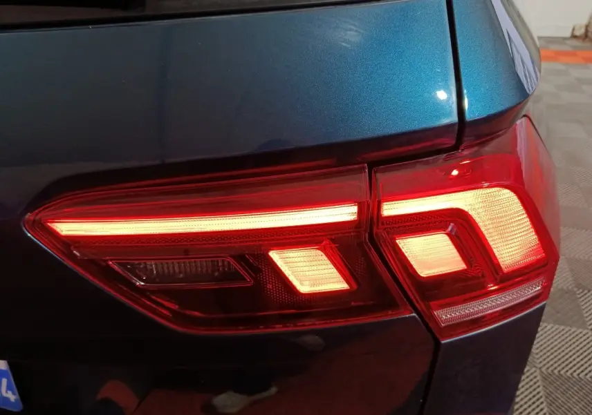Gros plan sur le feu arrière droit allumé d’un Volkswagen Tiguan bleu métallisé, avec détails lumineux rouges et blancs.