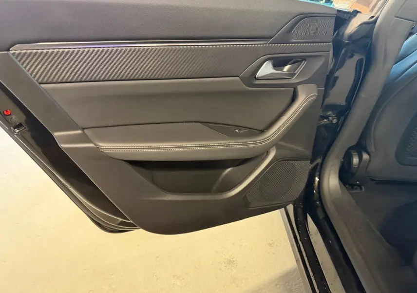 Vue intérieure du panneau de porte arrière gauche noir avec surpiqûres et insert effet carbone d'une Peugeot 508 SW 2024.