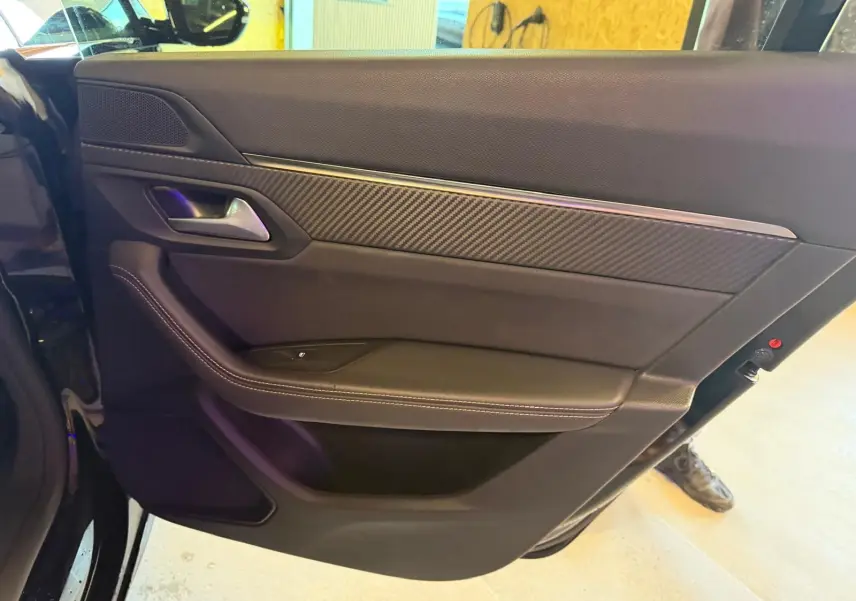 Vue rapprochée de la porte arrière gauche noire avec insert carbone et surpiqûres blanches du Peugeot 508 SW 2024.